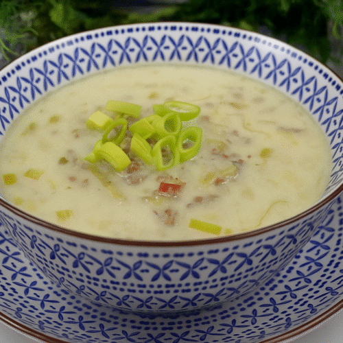 Eine Schale cremige Käse-Lauch-Suppe mit Hackfleisch, serviert in einer blau-weiß gemusterten Keramikschale auf passendem Teller, garniert mit frischen Lauchringen.