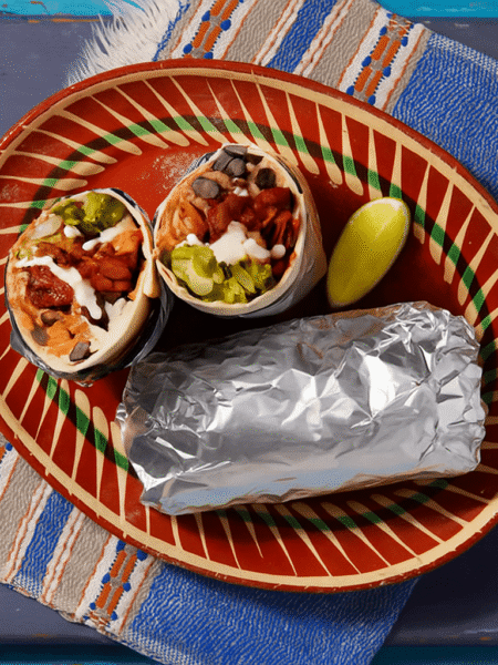 Pulled Jackfruit Burritos served on a colorful ceramic plate with lime wedge and foil wrap, showcasing the filling of jackfruit, black beans, lettuce, and sauce.