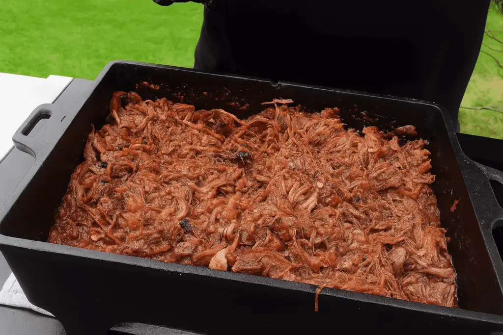 Pulled Beef in a Dutch oven after grilling, shredded and mixed with sauce, outdoors on a black table.