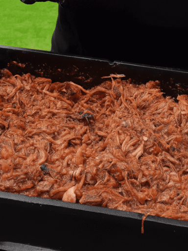 Pulled Beef in a Dutch oven after grilling, shredded and mixed with sauce, outdoors on a black table.