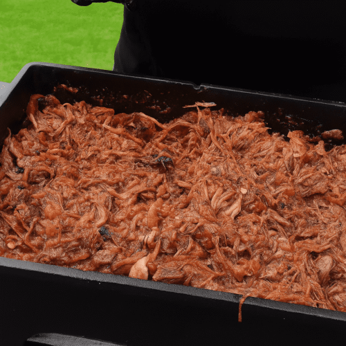 Pulled Beef in a Dutch oven after grilling, shredded and mixed with sauce, outdoors on a black table.