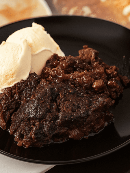 Schoko Kirsch Cobbler mit Vanilleeis auf einem schwarzen Teller – ein warmes, schokoladiges Dessert mit saftigen Kirschen und cremigem Eis.