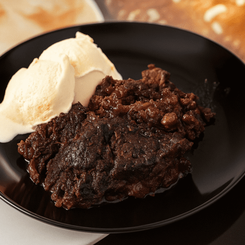 Schoko Kirsch Cobbler mit Vanilleeis auf einem schwarzen Teller – ein warmes, schokoladiges Dessert mit saftigen Kirschen und cremigem Eis.