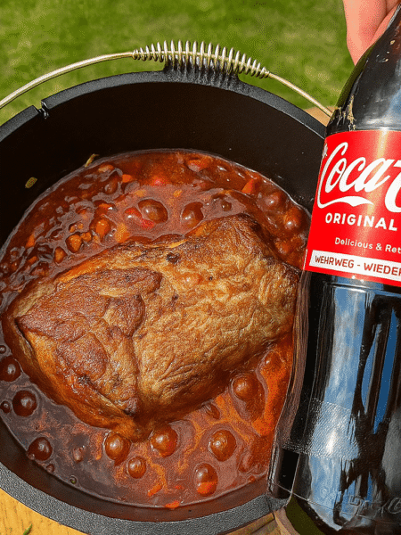 Geschmortes Colafleisch mit Cola, Sauerkirschen und BBQ-Sauce, serviert in einer gusseisernen Pfanne.