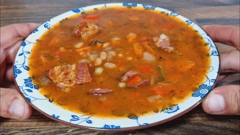 Ungarische Bohnensuppe mit geräuchertem Fleisch, weißen Bohnen, Paprika und Dill in einem tiefen Teller serviert.