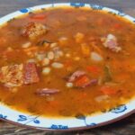 Ungarische Bohnensuppe mit geräuchertem Fleisch, weißen Bohnen, Paprika und Dill in einem tiefen Teller serviert.