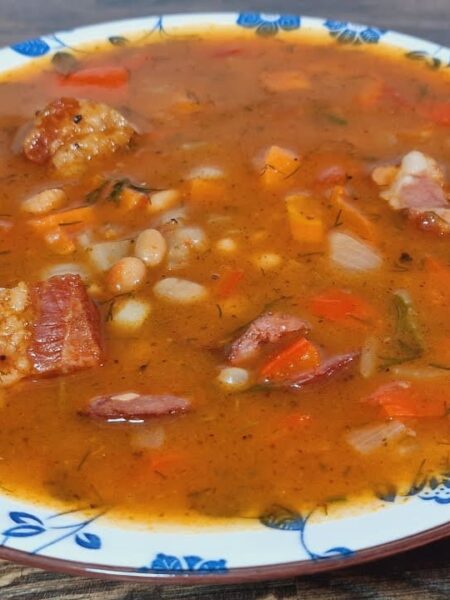Ungarische Bohnensuppe mit geräuchertem Fleisch, weißen Bohnen, Paprika und Dill in einem tiefen Teller serviert.