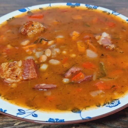 Ungarische Bohnensuppe mit geräuchertem Fleisch, weißen Bohnen, Paprika und Dill in einem tiefen Teller serviert.