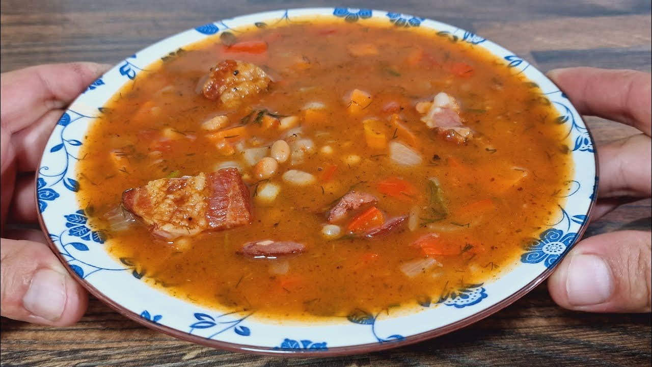 Ungarische Bohnensuppe mit geräuchertem Fleisch, weißen Bohnen, Paprika und Dill in einem tiefen Teller serviert.