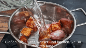 Fleisch vorkochen: Schneide die 500 g geräuchertes Fleisch oder Rippen in mundgerechte Stücke. Gib sie in einen großen Topf, füge 2 Liter Wasser hinzu und bringe alles zum Kochen. Reduziere dann die Hitze und lasse das Fleisch etwa 30 Minuten sanft köcheln. So wird es zart und gibt Geschmack an die Brühe ab.